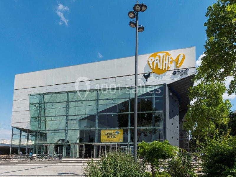Façade moderne d'un cinéma Pathé avec de grandes baies vitrées, entouré de végétation et éclairé par un ciel bleu.
