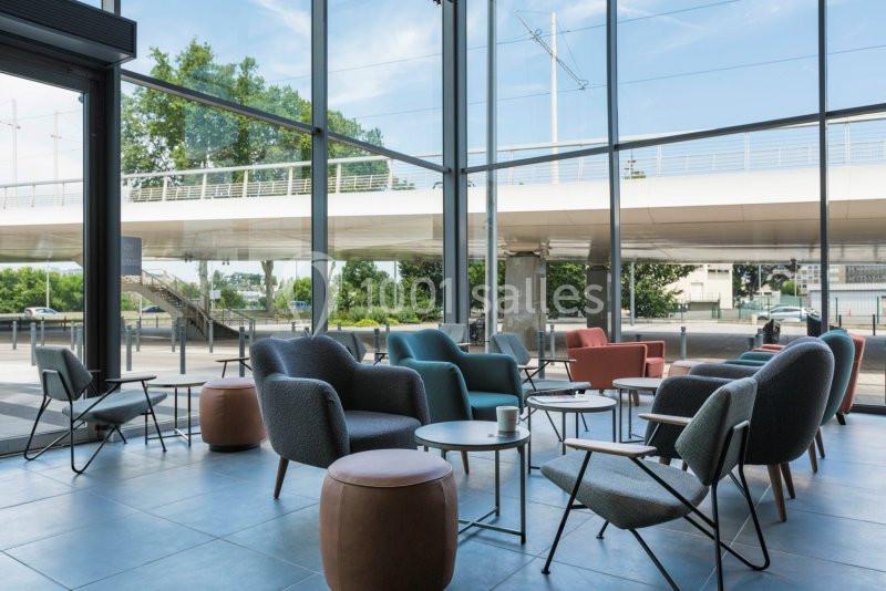 Espace intérieur lumineux avec fauteuils modernes, tables basses et vue sur un pont à travers de grandes baies vitrées.