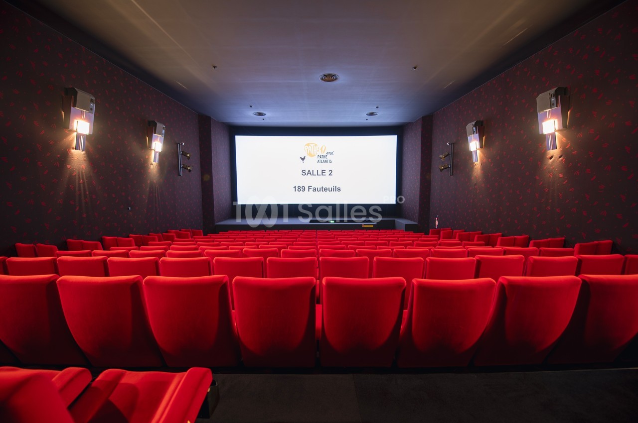 Salle de cinéma vide avec des fauteuils rouges alignés face à un grand écran affichant ’Salle 2, 189 fauteuils’.