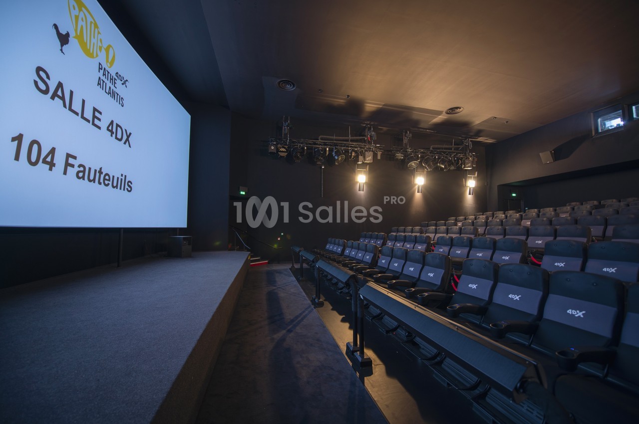 Salle de cinéma équipée de sièges 4DX, éclairée par des projecteurs, avec écran et 104 fauteuils visibles.
