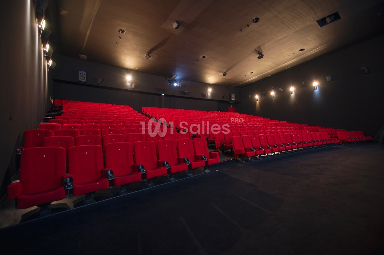 Salle de cinéma vide avec rangées de sièges rouges et éclairage tamisé.