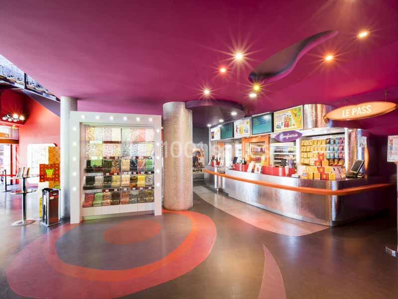 Intérieur d'un cinéma avec un comptoir de confiseries, un mur coloré et un éclairage chaleureux.