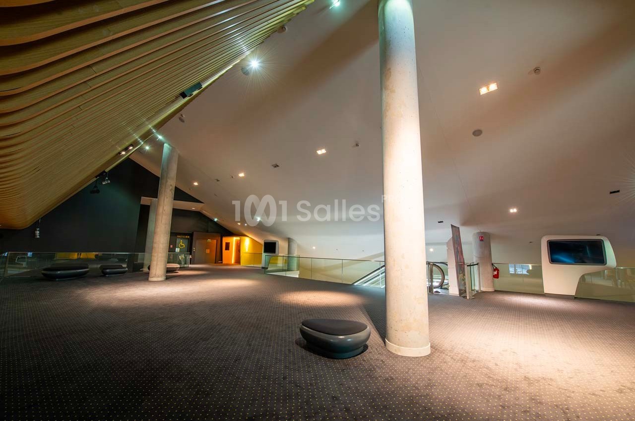 Intérieur spacieux et moderne avec plafond incliné, colonnes, escalier mécanique et éclairage tamisé.