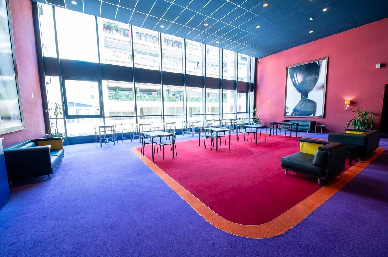 Salle lumineuse avec de grandes fenêtres, tapis coloré, mobilier moderne et une grande peinture murale.