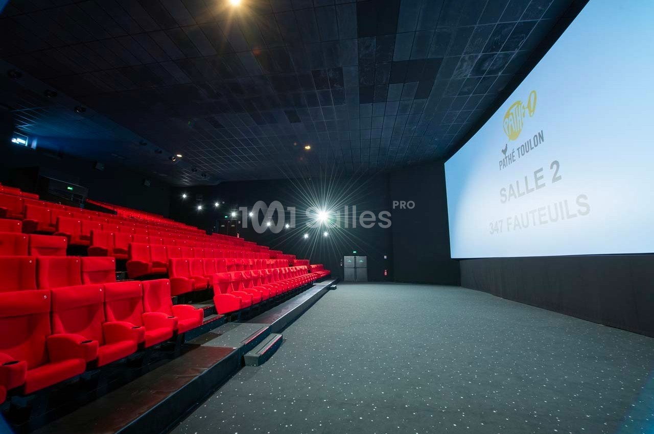 Salle de cinéma vide avec rangées de fauteuils rouges et écran affichant ’Salle 2, 347 fauteuils’.