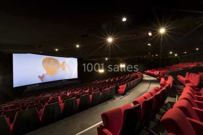 Salle de cinéma avec rangées de sièges rouges vides, grand écran allumé affichant un logo Pathé.