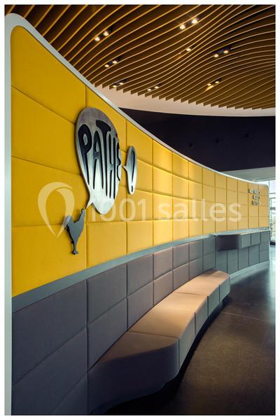 Mur jaune avec logo Pathé en relief, banquette grise incurvée en dessous et plafond à lames de bois.