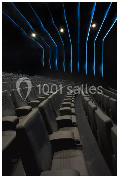Salle de cinéma sombre avec rangées de sièges en cuir gris et éclairage bleu au plafond.