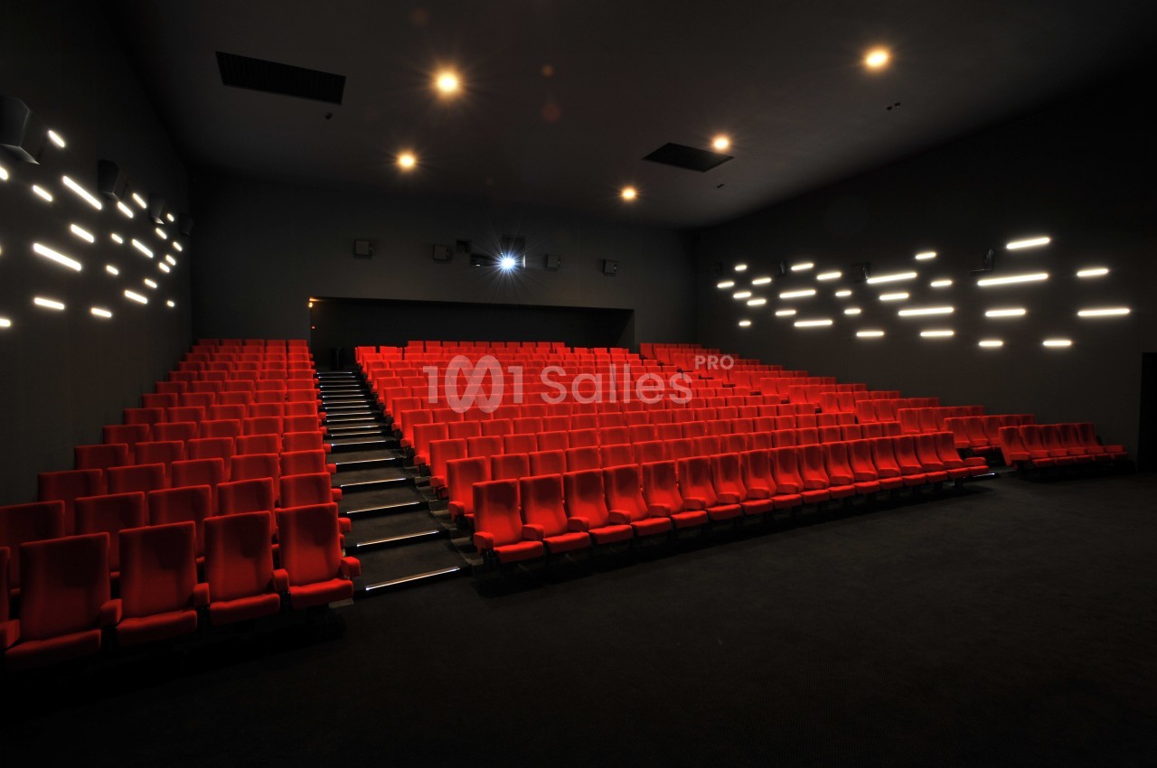 Salle de cinéma vide avec rangées de sièges rouges et éclairage mural discret.