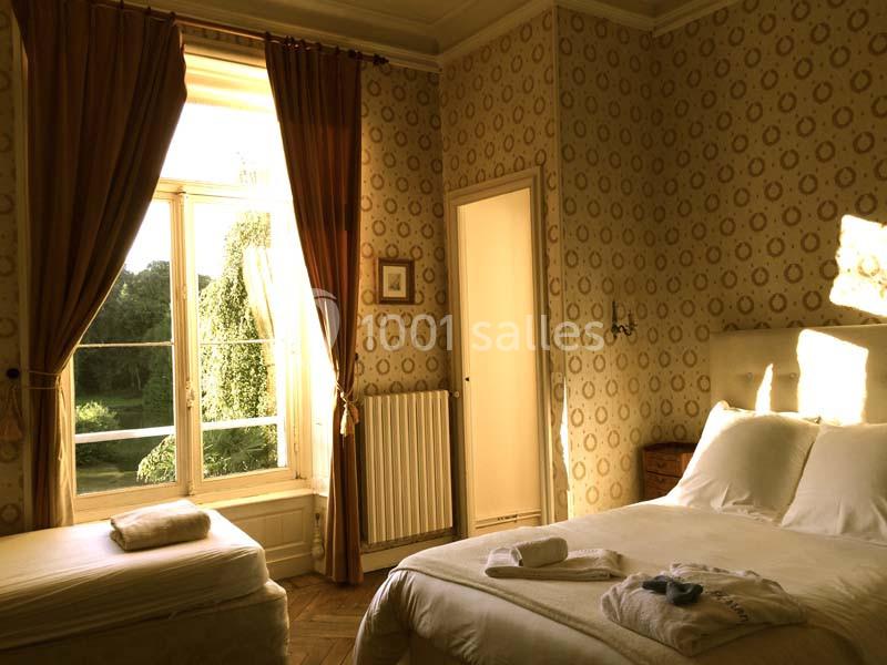 Chambre lumineuse avec lit double, lit simple, grandes fenêtres donnant sur un jardin et rideaux ouverts.