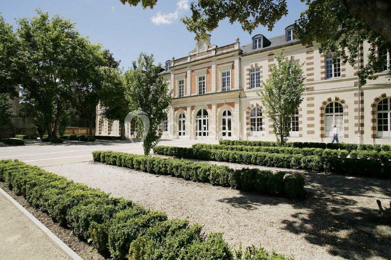 Façade d'un bâtiment historique en pierre entouré de jardins avec allées gravillonnées et arbres.