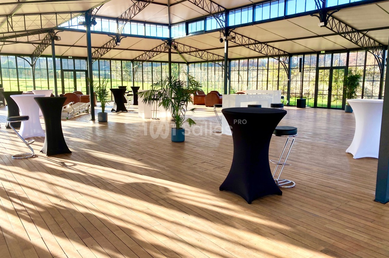 Salle lumineuse avec parquet, tables hautes noires et blanches, grandes baies vitrées donnant sur un espace vert.