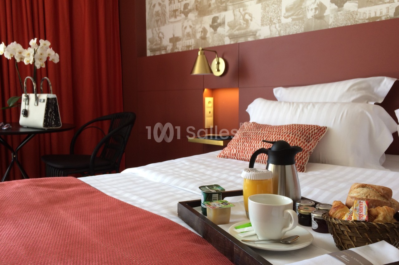 Chambre d'hôtel avec lit double, plateau de petit-déjeuner, mur rouge, rideaux assortis et décoration élégante.