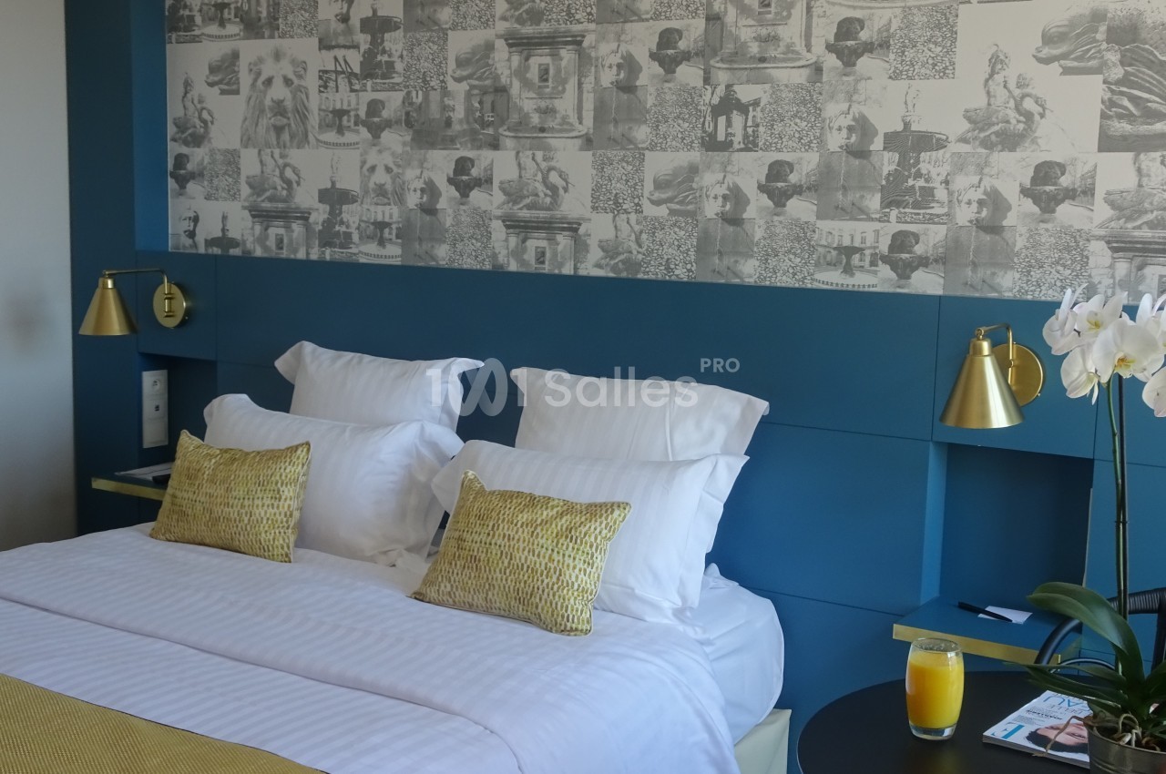 Lit double avec oreillers et coussins jaunes, éclairé par des lampes dorées, devant un mur décoré de motifs artistiques.