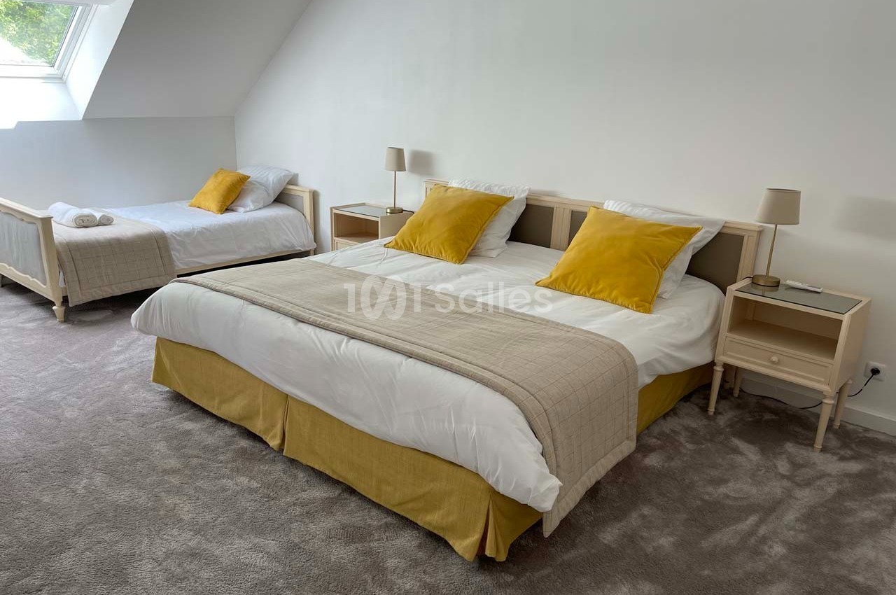 Chambre lumineuse avec un lit double, un lit simple, des coussins jaunes et une décoration sobre.