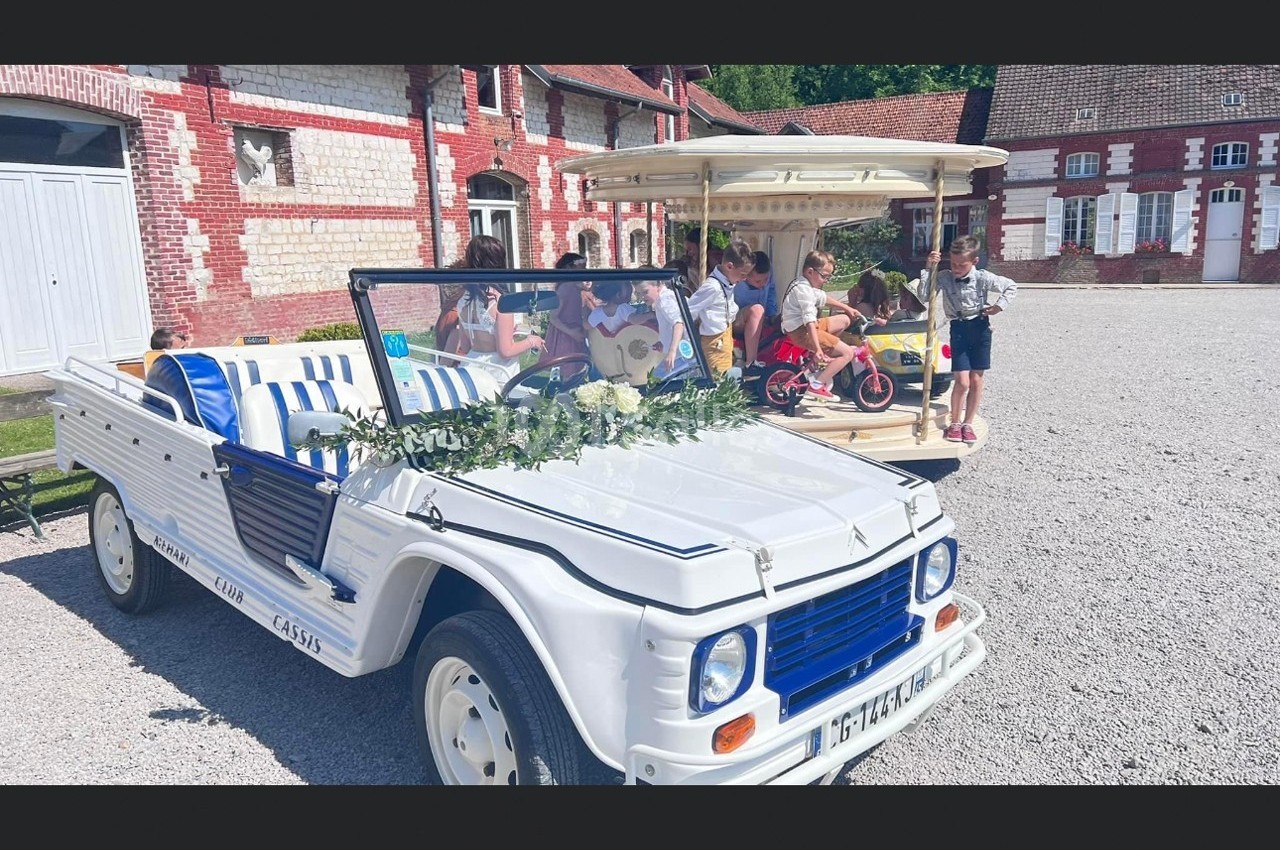 Voiture décapotable blanche décorée de fleurs devant un bâtiment en briques, avec des enfants jouant autour.