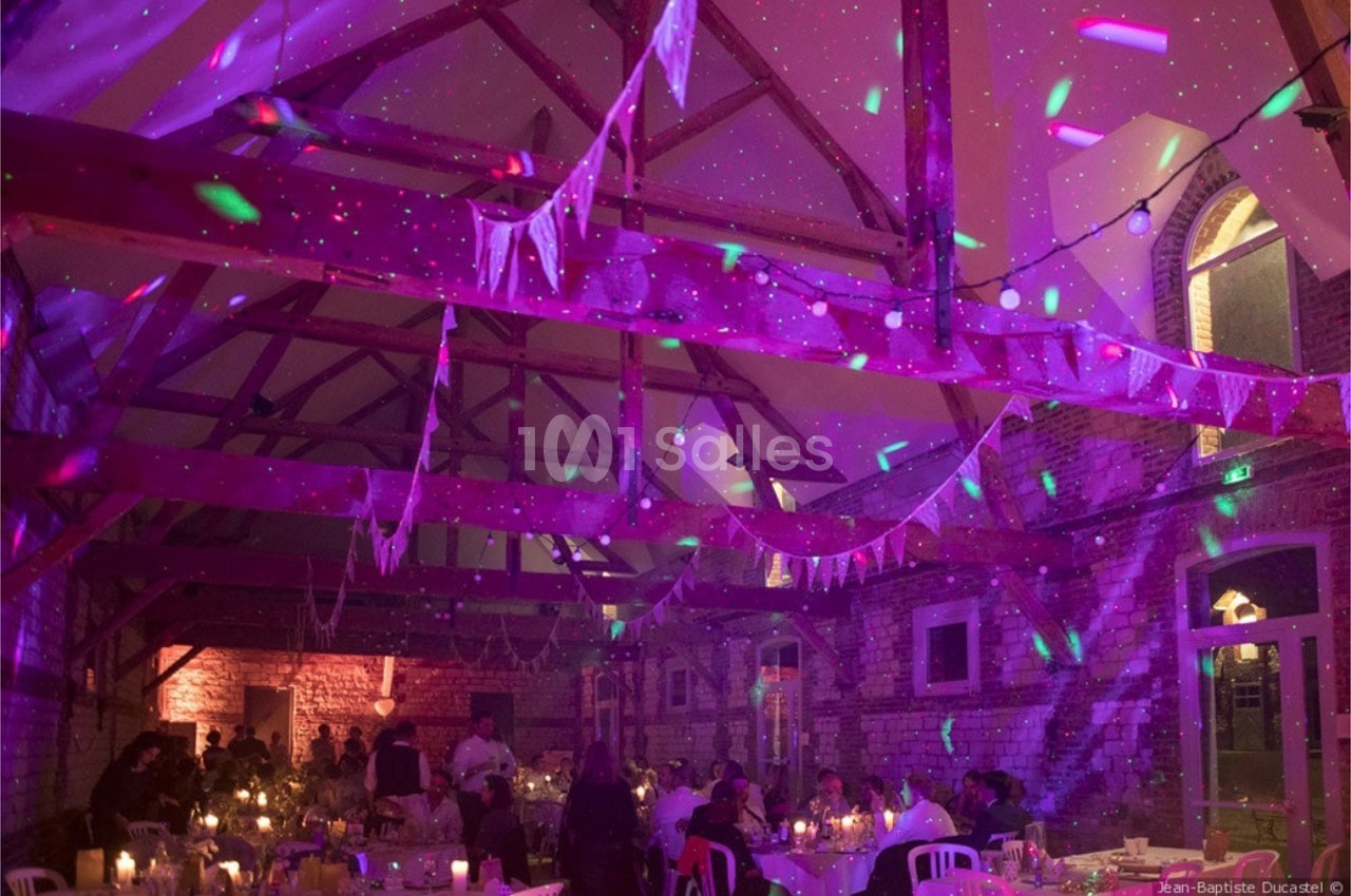 Salle de réception décorée avec des guirlandes et éclairages colorés, occupée par des convives à table.