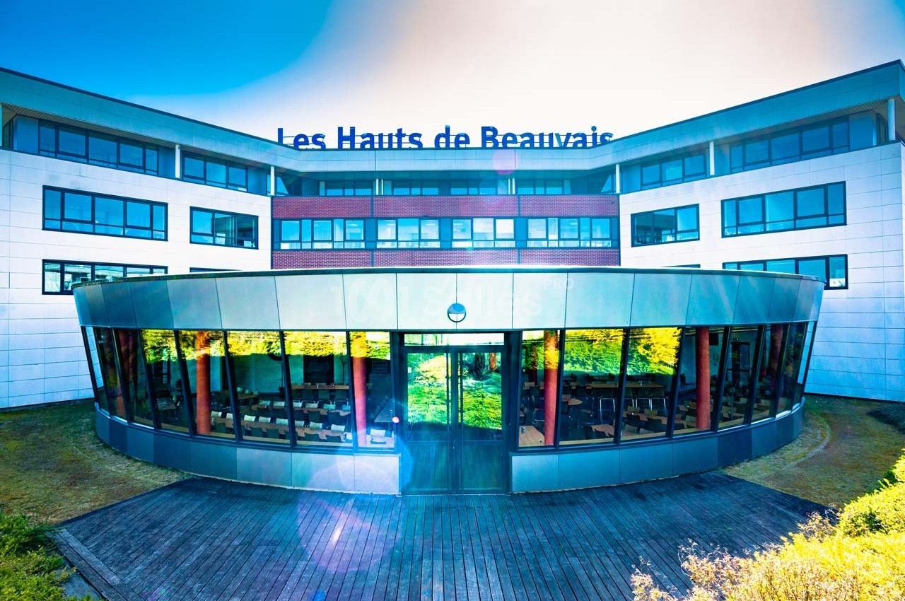 Bâtiment moderne avec façade vitrée réfléchissant des arbres, inscription ’Les Hauts de Beauvais’ visible en haut.