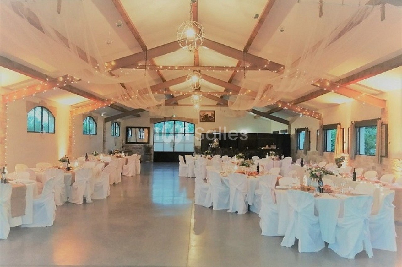 Salle de réception décorée avec des tables rondes, nappes blanches, guirlandes lumineuses et voilages suspendus.