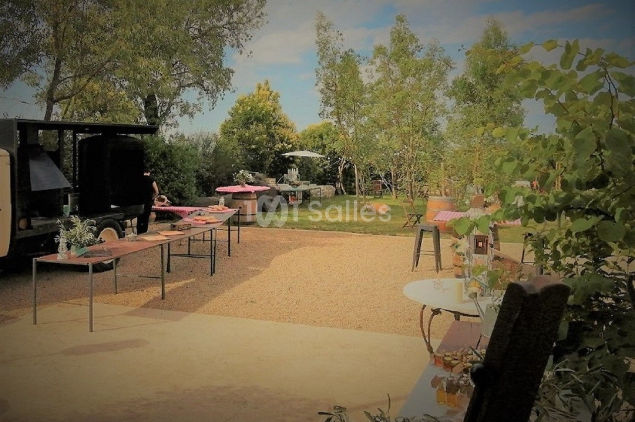 Espace extérieur aménagé avec tables, chaises et végétation, sous un ciel dégagé, pour un événement en plein air.