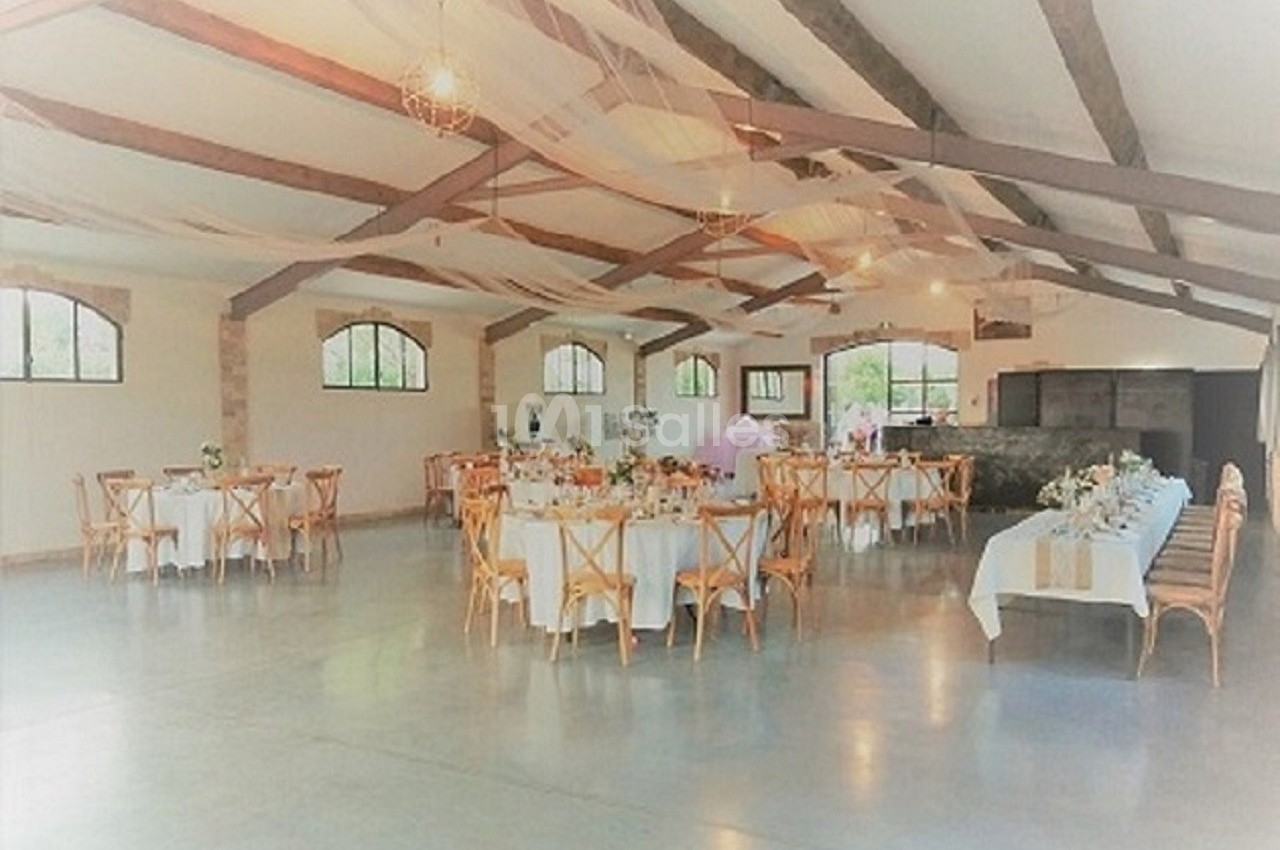 Salle de réception lumineuse avec tables rondes décorées, chaises en bois et poutres apparentes au plafond.