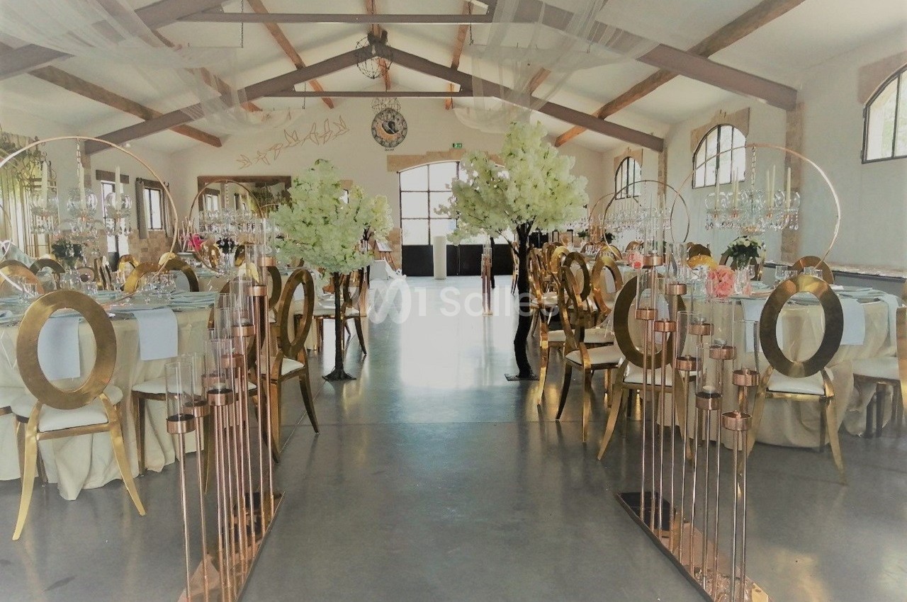 Salle de réception décorée avec des tables élégantes, des arches dorées et des compositions florales blanches.