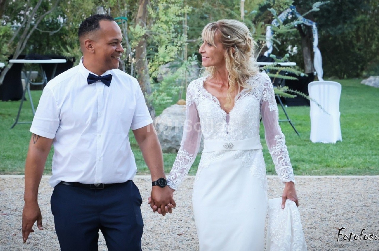 Un couple en tenue de mariage marche main dans la main dans un jardin.