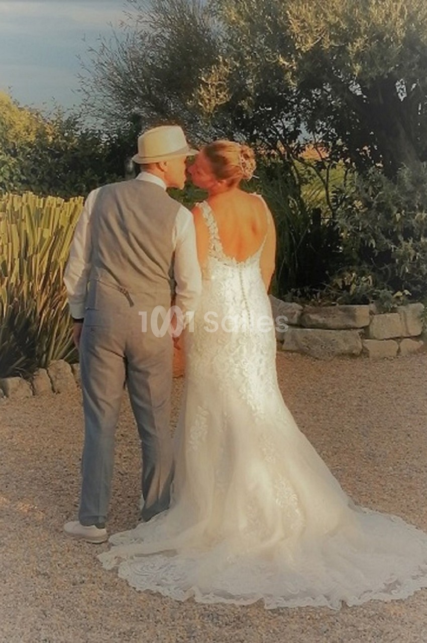 Un couple en tenue de mariage se tient la main et s'embrasse dans un jardin ensoleillé.