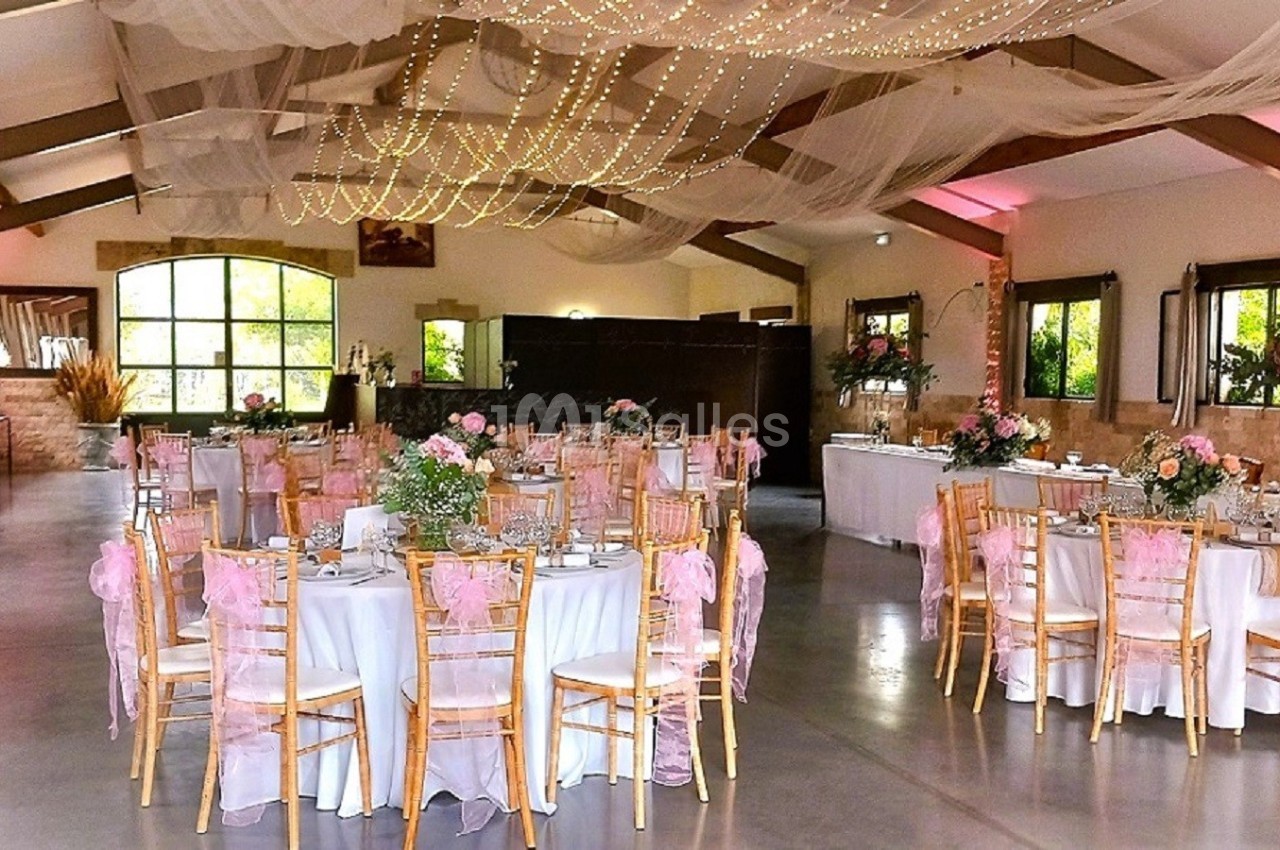 Salle de réception décorée avec des tables rondes, des chaises dorées et des guirlandes lumineuses suspendues au plafond.
