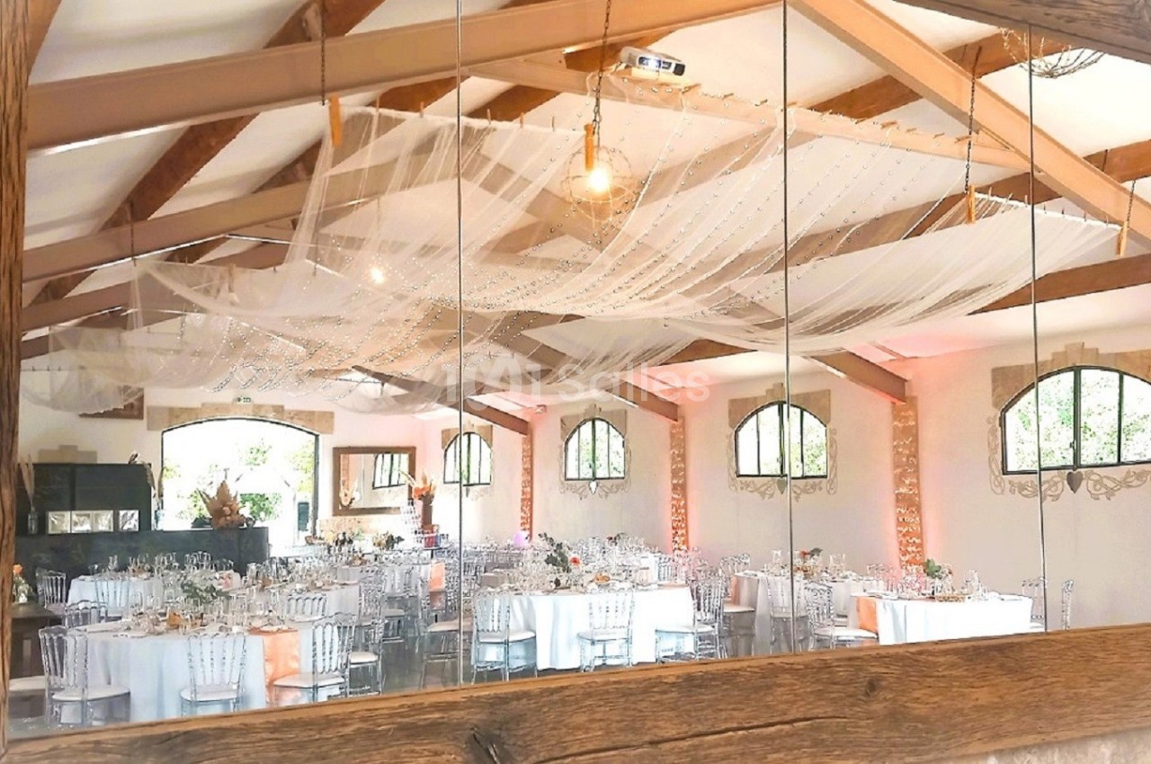 Reflet d'une salle de réception décorée avec des tables dressées, des voilages suspendus et des poutres apparentes.