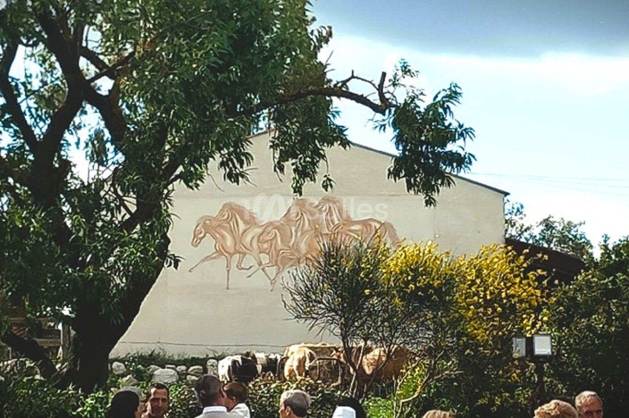 Fresque représentant des chevaux sur un mur blanc, entourée d'arbres et de végétation, avec des personnes au premier plan.