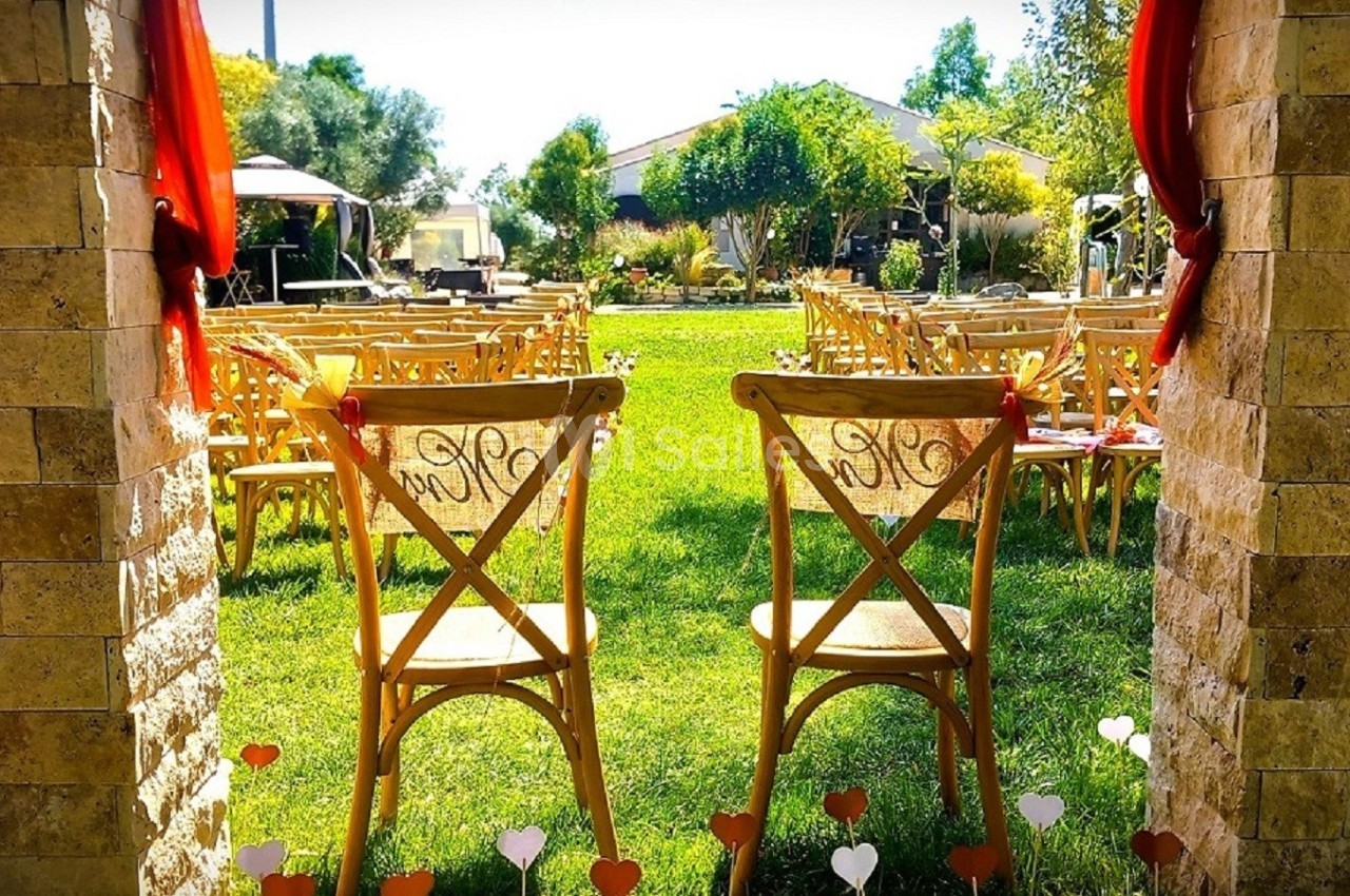 Chaises en bois alignées sur une pelouse pour une cérémonie en extérieur, encadrées par deux colonnes en pierre.