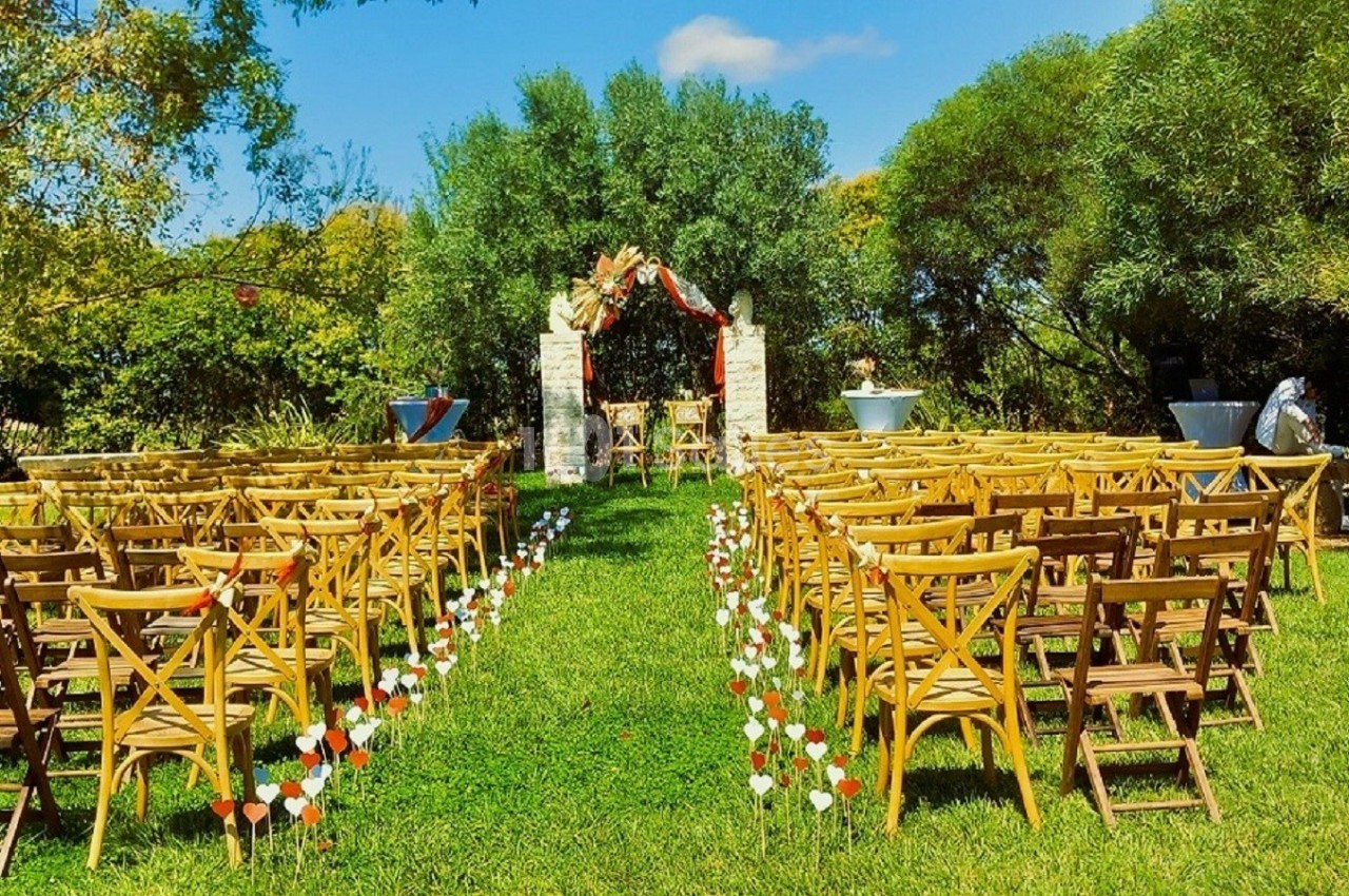 Chaises en bois disposées en rangées sur une pelouse, face à une arche décorée pour une cérémonie en extérieur.