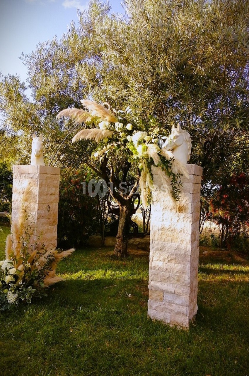 Deux colonnes en pierre décorées de fleurs et de feuillages, placées dans un jardin arboré.