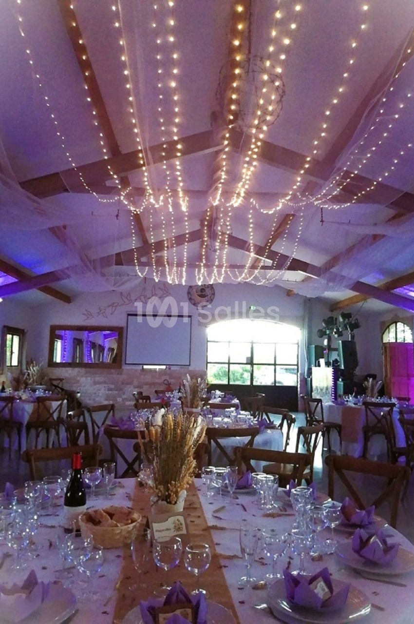 Salle de réception décorée avec des guirlandes lumineuses suspendues, tables dressées et ambiance chaleureuse.