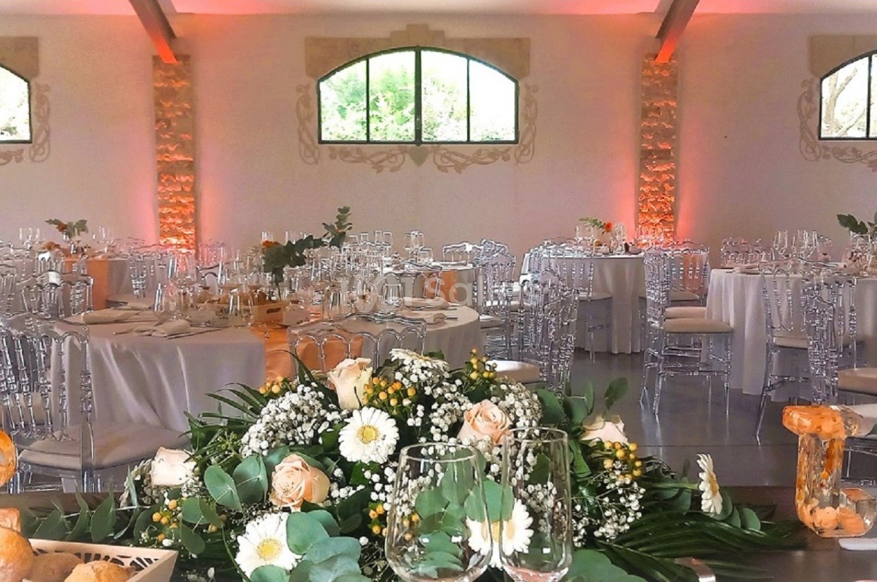 Salle de réception décorée avec des tables rondes, nappes blanches, chaises transparentes et compositions florales.