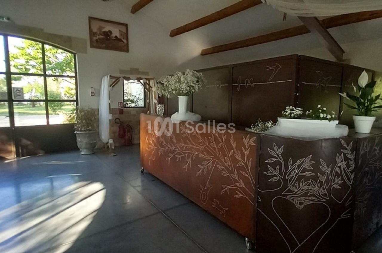 Comptoir en bois décoré de motifs gravés, situé dans une salle lumineuse avec de grandes fenêtres et des plantes.