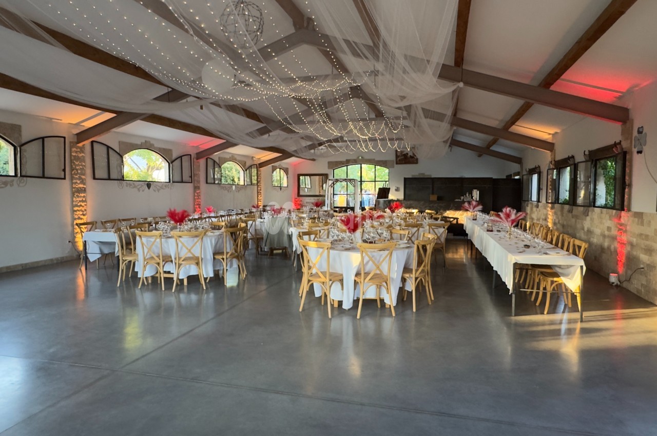Salle de réception décorée avec des tables dressées, des chaises en bois et un plafond orné de voilages et lumières.