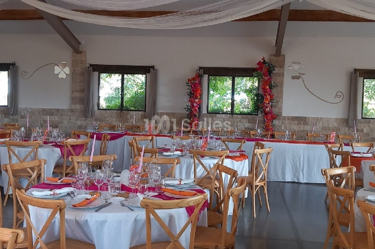 Salle de réception décorée avec des tables rondes dressées, nappes blanches et accents colorés, sous un plafond drapé.