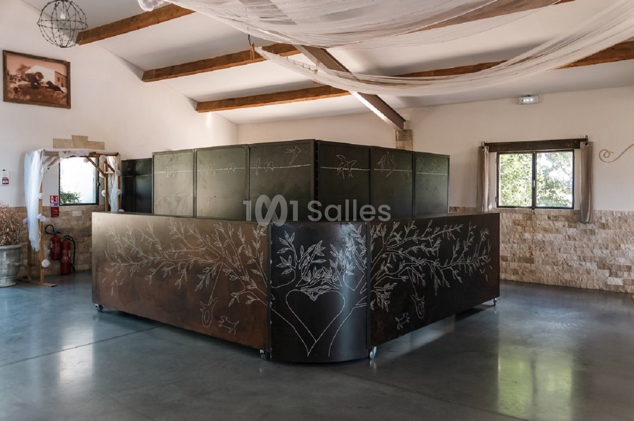 Comptoir en métal décoré de motifs gravés, installé dans une grande salle lumineuse avec poutres apparentes.
