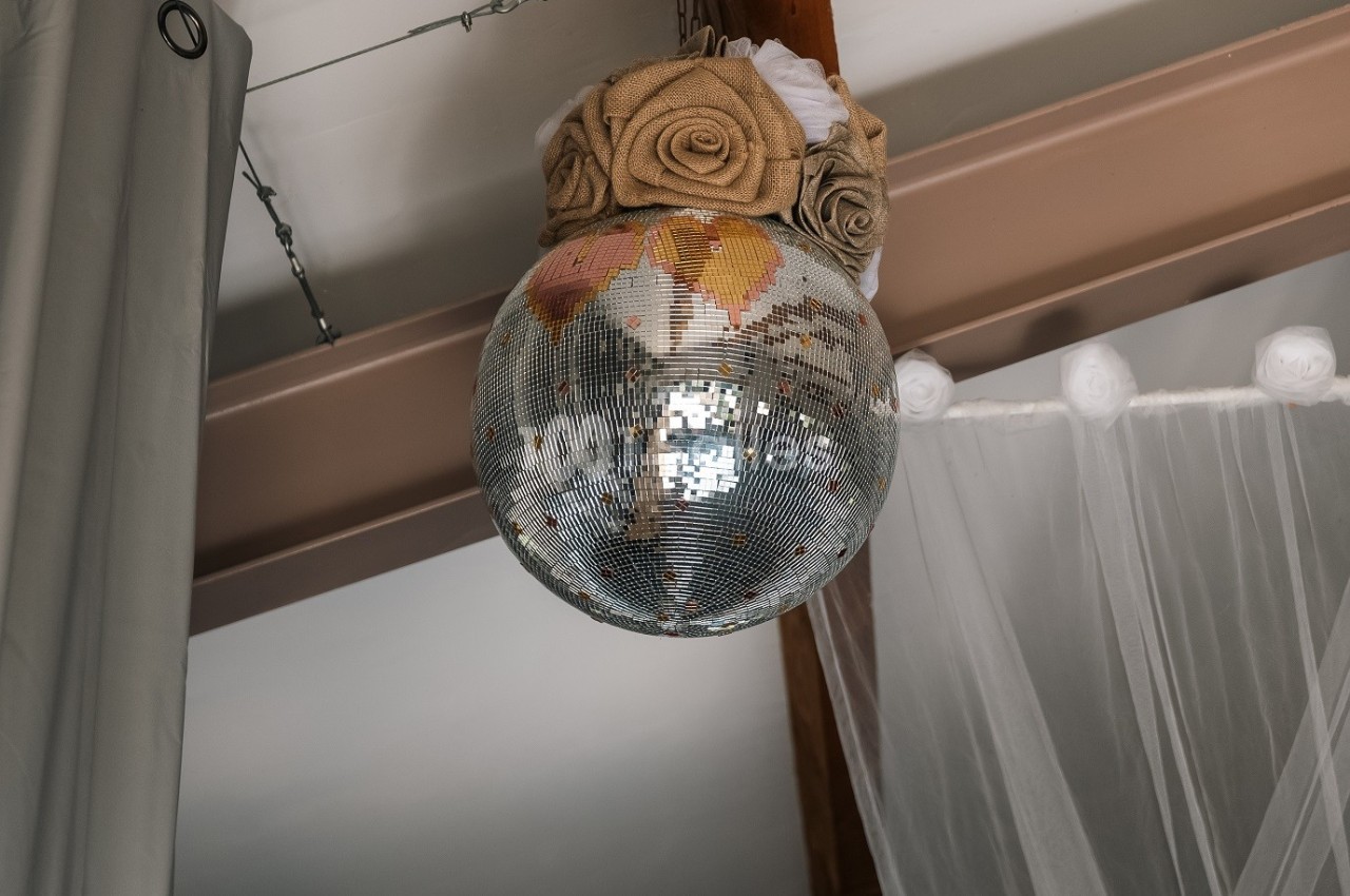 Boule à facettes décorée de roses en tissu suspendue à une poutre dans un intérieur lumineux.