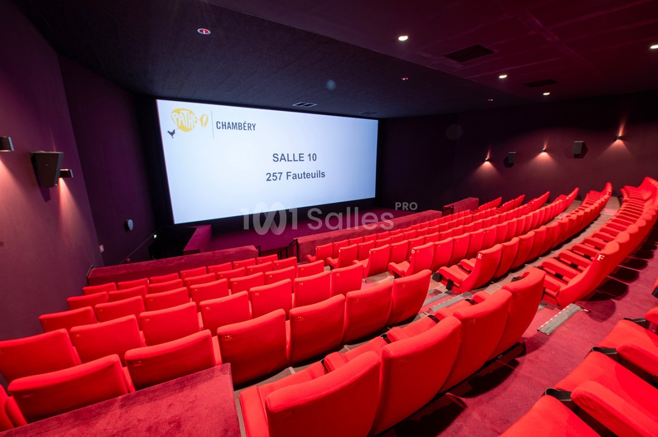 Salle de cinéma vide avec des sièges rouges, un écran affichant ’Salle 10, 257 fauteuils’ et un éclairage tamisé.