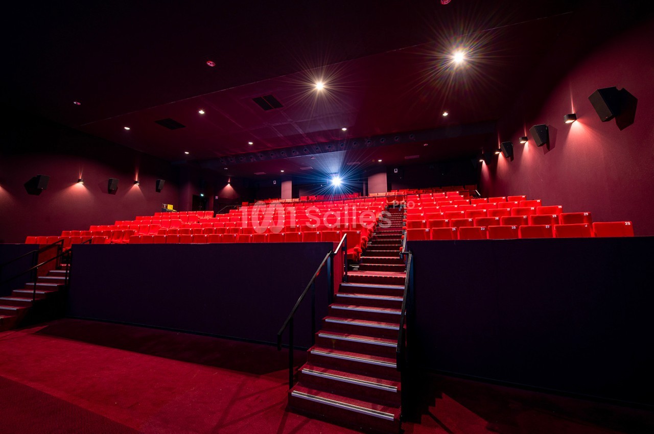 Salle de cinéma vide avec des rangées de sièges rouges, éclairée par des lumières tamisées.