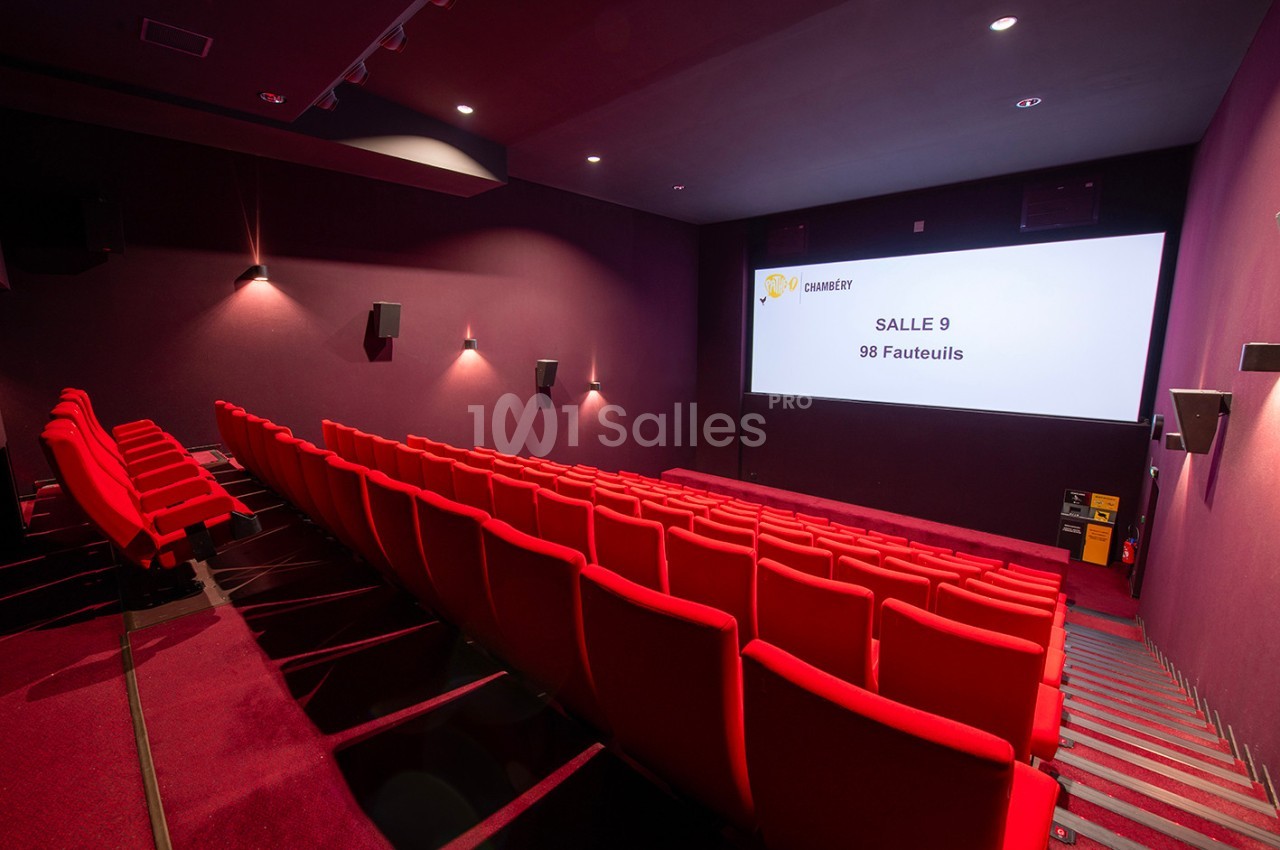 Salle de cinéma vide avec des rangées de fauteuils rouges et un écran affichant ’Salle 9, 98 fauteuils’.