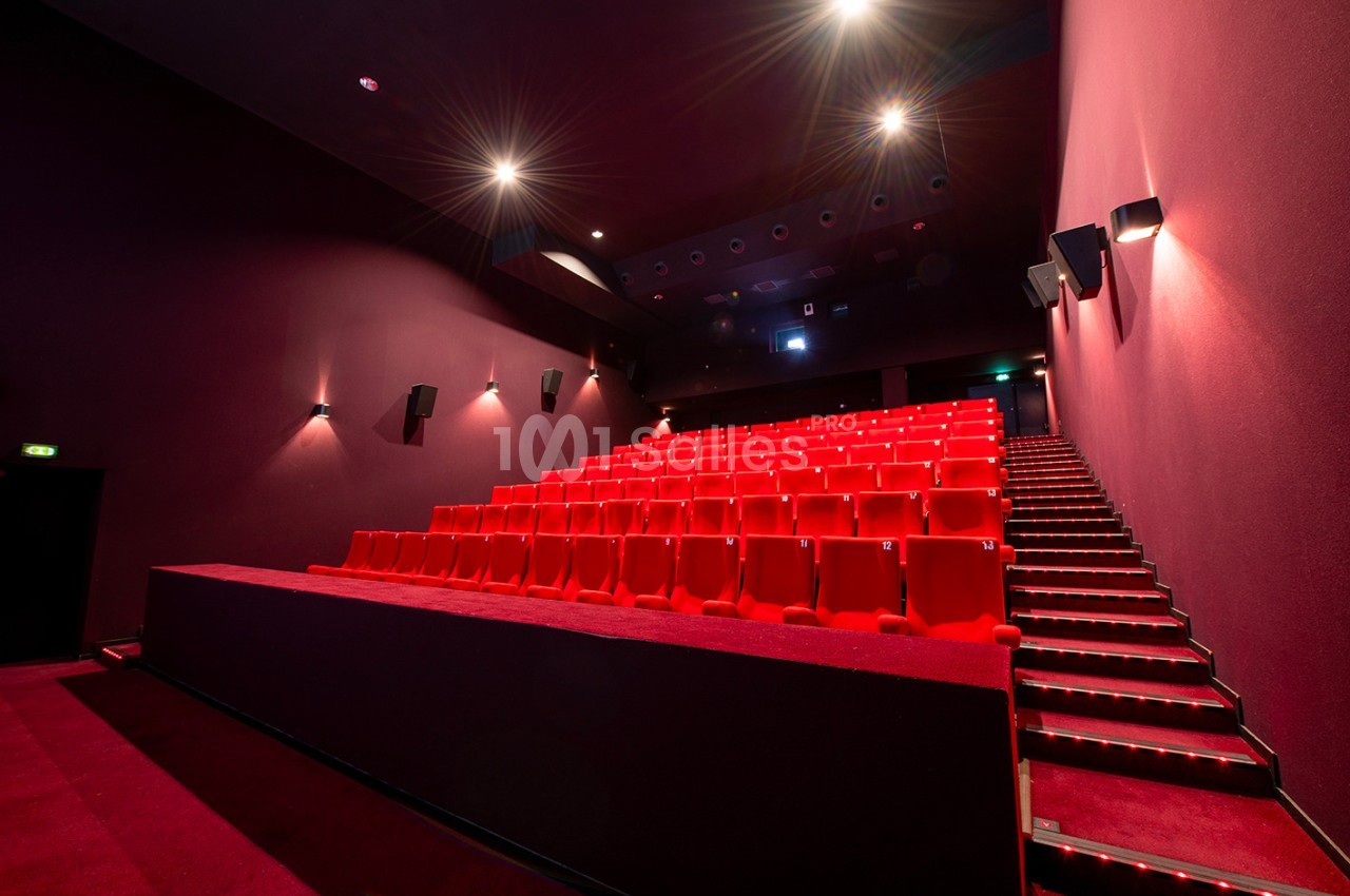 Salle de cinéma vide avec des rangées de sièges rouges et un éclairage tamisé.