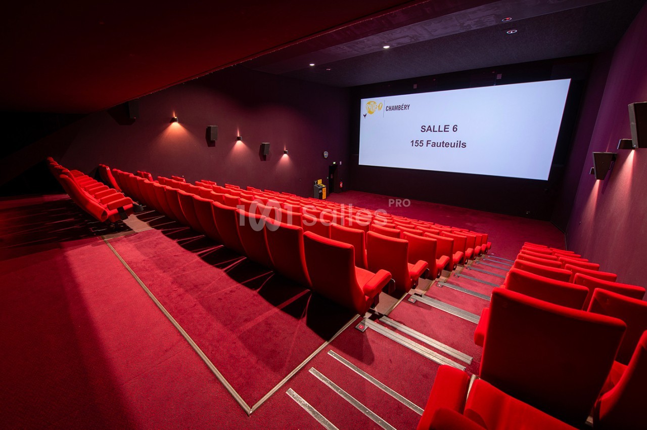 Salle de cinéma vide avec des sièges rouges, un écran affichant ’Salle 6, 155 fauteuils’ et un éclairage tamisé.