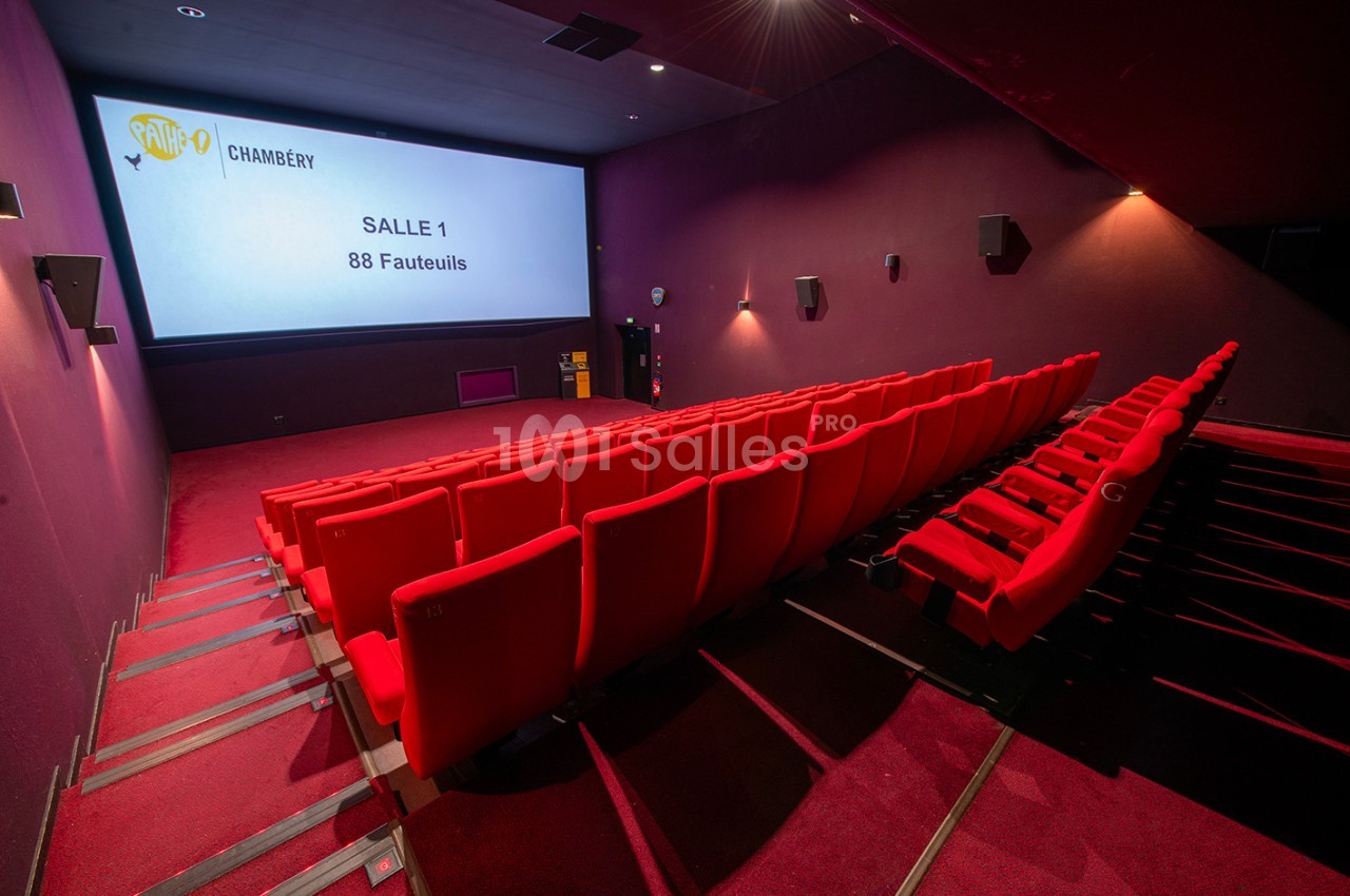 Salle de cinéma vide avec des sièges rouges, un écran affichant ’Salle 1, 88 fauteuils’ et des murs violets.