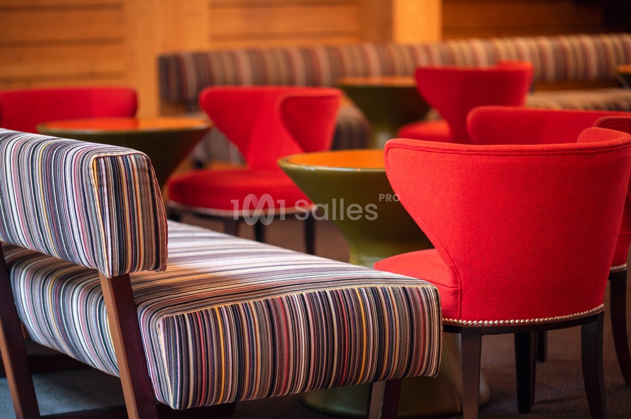 Chaises rouges et banquettes rayées entourant des tables rondes dans un espace intérieur chaleureux.