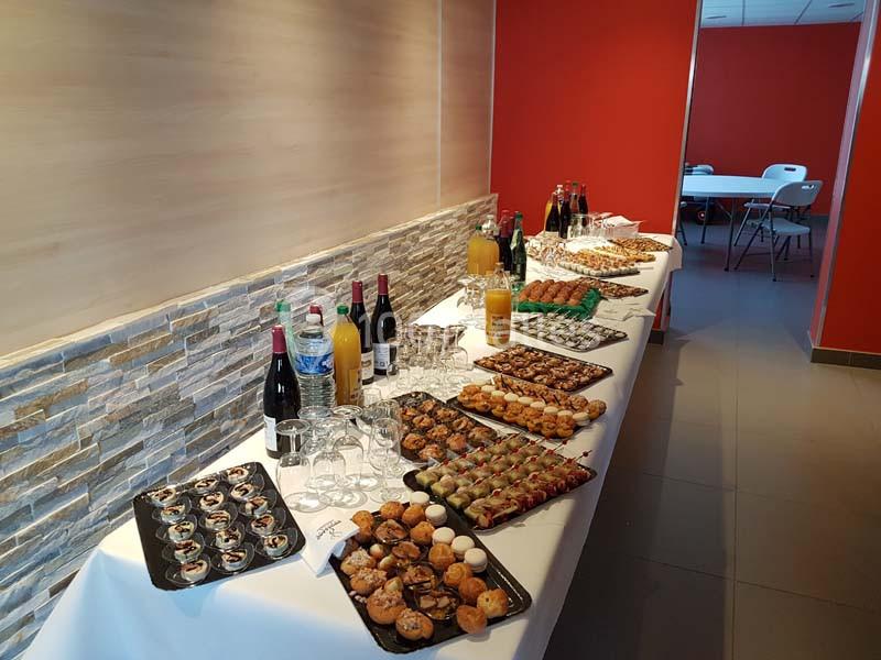 Buffet avec assortiments de bouchées salées et sucrées, boissons variées, disposé sur une table dans une salle.