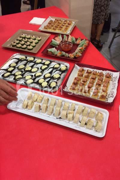 Plateaux de bouchées salées variées disposés sur une table rouge, avec quelques personnes en arrière-plan flou.